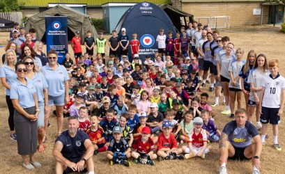 A large group photo of attending children and adults gathered outdoors on a grassy area, with Royal Air Force Benevolent Fund banners and pop-up tents in the background.